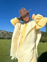 Ruana color crema tejida en lana merino, con flecos y bolsillos frontales.