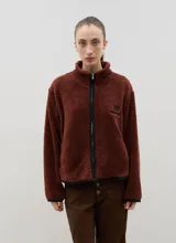 Campera de sherpa color beige con cuello alto, cierre frontal completo y bordado a contra tono en el pecho.