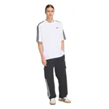 Remera Adidas de corte holgado, color blanco, con las icónicas tres tiras negras en las mangas y logo del Trifolio bordado en el pecho.