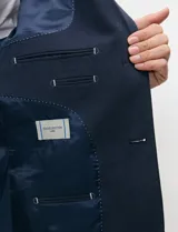 Blazer de medio forro azul marino confeccionado en mezcla de algodón y lino, con silueta estructurada, solapas de muesca, cierre frontal de dos botones y bolsillos con solapa.
