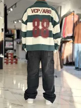 Buzo polo de rayas horizontales en gris oscuro y blanco, con cuello camisero, cierre frontal parcial y corte oversize. Presenta un gran número 88 estampado en la espalda en color bordó junto con la inscripción VCP/ARG.