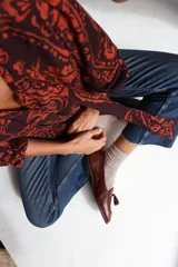 Camisa de lino con estampado paisley en tonos marrón y naranja, cuello con lazos integrados, mangas largas con frunces en hombros y puños elásticos, y cierre frontal con botones de coco.