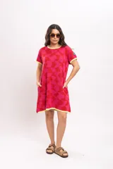 Vestido corto tejido de punto con diseño geométrico abstracto en tonos rojo y fucsia, cuello redondo, mangas cortas y bolsillos laterales, con detalles en amarillo en el cuello, puños y ruedo.