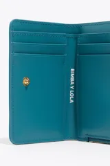 Billetera compacta de estructura blanda en color turquesa, con cierre de cremallera superior y logo metálico dorado en el frente.