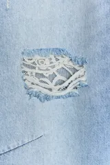 Jeans de tiro medio con corte baggy, pernera holgada que se estrecha hacia el tobillo. Presenta diseño de cinco bolsillos, cierre frontal con cremallera y botón, y detalles de roturas con aplicaciones de encaje en el frente.