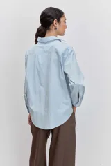 Camisa de algodón color celeste claro, con cuello clásico, cierre frontal de botones y detalle de tachas metálicas plateadas distribuidas por toda la prenda.