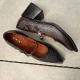 Zapato tipo Mary Jane de cuero vacuno con textura grabada, color marrón oscuro. Presenta una puntera cuadrada, taco bloque de madera y una tira con hebilla metálica sobre el empeine.