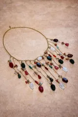 Collar de cadena dorada con múltiples dijes colgantes de piedras naturales en tonos rojos, verdes, blancos y transparentes, con detalles de pequeñas cuentas y eslabones metálicos.