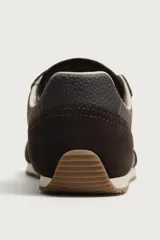 Zapatilla deportiva estilo barefoot, color marrón, con diseño de paneles en combinación de materiales y detalles en serraje. Cuenta con puntera redondeada y ancha, cordones en color crema y suela fina de goma flexible en contraste.