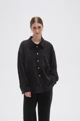 Camisa de pana negra con cuello clásico, cierre frontal de botones y bolsillo en el pecho.