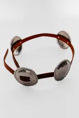 Cinturón marrón de cuero con apliques metálicos plateados de forma ovalada con borde irregular.