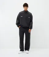 Pantalón deportivo de corte recto y estilo holgado, color negro con una línea vertical blanca en los laterales. Cuenta con cintura elástica con cordón de ajuste y bolsillos laterales.