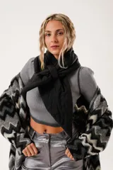Bufanda negra con diseño capitoné acolchado y costuras decorativas. Presenta una terminación en pico y un sistema de ajuste mediante una tira integrada para cruzarla.
