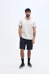 Chomba de piqué color beige, de manga corta, con cuello polo y puños tejidos con líneas en contraste, y logo bordado en el pecho.