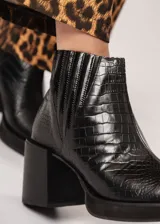 Botín negro de cuero con elástico lateral y cierre interno. Tiene plataforma delantera de 2 cm y taco de 8 cm.