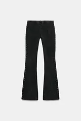 Pantalón de tiro medio con cintura elástica y corte acampanado. Presenta un acabado lavado y detalle de tachas metálicas a lo largo de las costuras laterales.