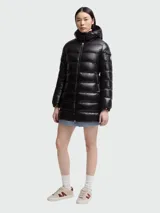 Campera puffer de corte largo con acabado brillante, cierre frontal, capucha integrada y bolsillos laterales con cierre. Presenta el logo de la marca en la manga izquierda.
