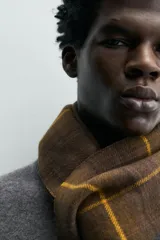 Bufanda de tejido doble cara con tacto suave, diseño a cuadros en tonos marrón y líneas amarillas, con acabado de flecos en los extremos.