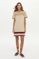 Vestido corto de tejido de punto en color beige, con cuello redondo y mangas cortas. Presenta detalles de rayas en tono bordó, marrón y blanco en el pecho, cuello, mangas y en el borde inferior.