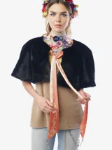 Capa corta de piel sintética negra, con diseño reversible que presenta un forro de satén con estampado floral. Incluye un lazo frontal estampado con borlas decoradas con cristales.