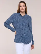 Camisa de rayón azul marino con estampado de lunares pequeños en tonos claros, cuello camisero, cierre frontal de botones, mangas largas y ruedo curvo asimétrico más largo en la espalda.
