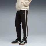 Pantalón de jogging Puma color negro con franjas laterales en color crema. Presenta cintura elástica con cordón ajustable, puños acanalados en los tobillos y logo de la marca bordado en la parte superior.