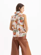 Blusa Pop de voile de seda y algodón, color blanco con estampado exclusivo de motivos frutales y florales. Presenta silueta en línea A, calce holgado, cuello alto fruncido con volados y escote profundo con volados caracol al frente.