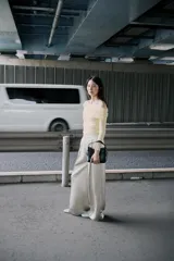 Bolso tipo mini shopper de diseño estructurado en color crema, con silueta en forma de V en la parte superior y asa de mano fija. Incluye detalles de pespuntes visibles y herrajes metálicos en tono dorado.