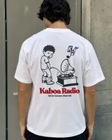 Remera blanca de manga corta con estampado gráfico en la espalda que incluye un personaje ilustrado, un gramófono y la inscripción "Kaboa Radio".