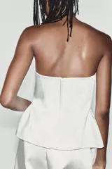 Top palabra de honor de tejido satinado blanco, con escote recto y diseño con bajo tipo peplum y costuras marcadas.