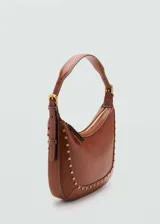 Bolso de hombro tipo hobo color marrón, confeccionado en efecto piel con detalle de tachuelas metálicas doradas en los bordes. Cuenta con asa ajustable con hebilla y cierre de cremallera superior.
