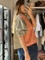 Blusa bicolor de pana elastizada con mangas cortas abullonadas, cuello redondo amplio y diseño estampado con combinación de tela roja con motivos florales pequeños y mangas y cuello en tono gris con estampa similar.