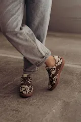 Zapatillas de cuero con estampado que simula pelo de vaca o manchas marrones y blancas. Tienen detalles en cuero marrón liso, cordones marrones y suela de goma color caramelo.