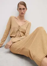 Cardigan de punto color tostado, con cuello en pico, diseño corto y cierre frontal mediante lazos. Posee mangas largas y un tejido de textura ligera.