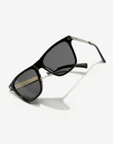 Lentes de sol unisex con marco cuadrado negro, patillas metálicas plateadas y cristales polarizados oscuros.