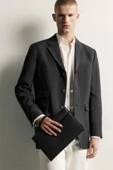 Bolso tipo sobre negro con acabado texturizado y detalle de banda horizontal lisa. Cuenta con compartimento principal con cierre de cremallera, bolsillo frontal plano, asa de mano corta y organizador interno para tarjetas.