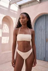Conjunto de bikini color blanco marfil con corpiño tipo banda con tirante halter y bombacha de corte clásico.