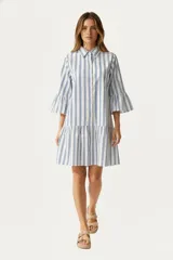 Vestido corto de algodón con estampado de rayas verticales azules y blancas. Presenta cuello camisero, cierre frontal con botones, mangas tres cuartos con volados en los puños y un corte holgado con falda con volado en la base.