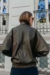 Cazadora estilo bomber color marrón oscuro, con efecto piel, cuello subido y manga larga. Tiene bolsillos delanteros con cierre de cremallera y acabados elásticos en puños y bajo. El cierre frontal es con cremallera y botones a presión ocultos.