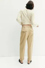 Pantalón chino de tiro medio, corte recto y holgado, con pinzas en la parte delantera. Presenta bolsillos laterales, falsos bolsillos traseros con solapa y bajo con dobladillo vuelto. Cierre frontal con cremallera y botones.