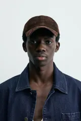 Gorra de béisbol color marrón oscuro, confeccionada en material con textura de ante o nobuk. Presenta visera curva y ojales metálicos a los lados para ventilación.