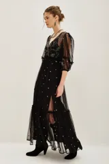 Vestido midi de tul negro con bordados brillantes y pedrería en el escote. Presenta mangas abullonadas, corte imperio y falda con volado en el ruedo. Incluye viso interior.