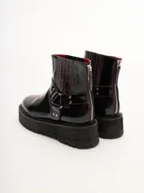 Bota corta de cuero negro tipo biker, con suela track de goma, plataforma, costuras y bordados decorativos en hilo rojo. Presenta tiras con hebillas metálicas y cierre en la parte trasera.