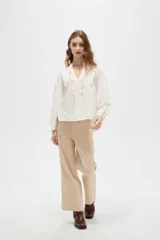 Blusa de viscosa color blanco, con cuello en V, detalles de volados y frunces en el frente, y mangas largas abullonadas con puños ajustados.