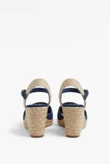 Sandalia de plataforma con cuña de yute y suela texturizada, color beige. Cuenta con puntera cerrada, diseño destalonado y tira ajustable al tobillo con hebilla metálica.