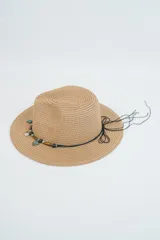 Sombrero de paja tejido color caqui, con ala ancha y copa tipo fedora. Está decorado con una cinta negra adornada con cuentas de madera, dijes turquesa en forma de hoja y dije de caracol.