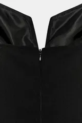 Vestido corto negro de escote en pico con tirantes finos y detalle de lazo blanco en el centro del pecho. Presenta un diseño ajustado con cierre de cremallera oculta en la espalda.