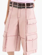 Bermuda de cuero ovino color rosa pálido con efecto 'brush off' (costuras y bordes desgastados en tono rojizo). Presenta un corte ancho y bolsillos cargo grandes en los laterales. Incluye dos cinturones finos ajustables con hebillas de metal.