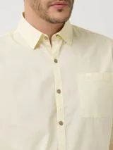 Camisa de manga larga RKF modelo Galiton, color amarillo, confeccionada en popelina 100% algodón orgánico. Cuenta con cuello camisero, botones de madera, un bolsillo frontal en el pecho con logo bordado y mangas ajustables.