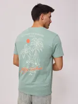 Remera negra de algodón con estampado en la espalda con palmeras, tabla de surf y texto en color blanco y fucsia.